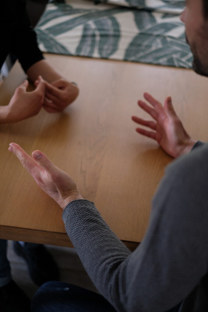 Les mains d'un médiateur parlant à une autre personne posée sur une table ouverte vers l'extérieur